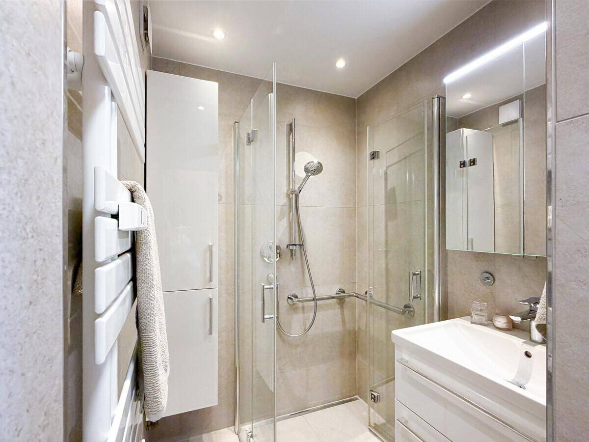 Modernes Badezimmer mit begehbarer Dusche, Handtuchheizkörper und hellen Fliesen.