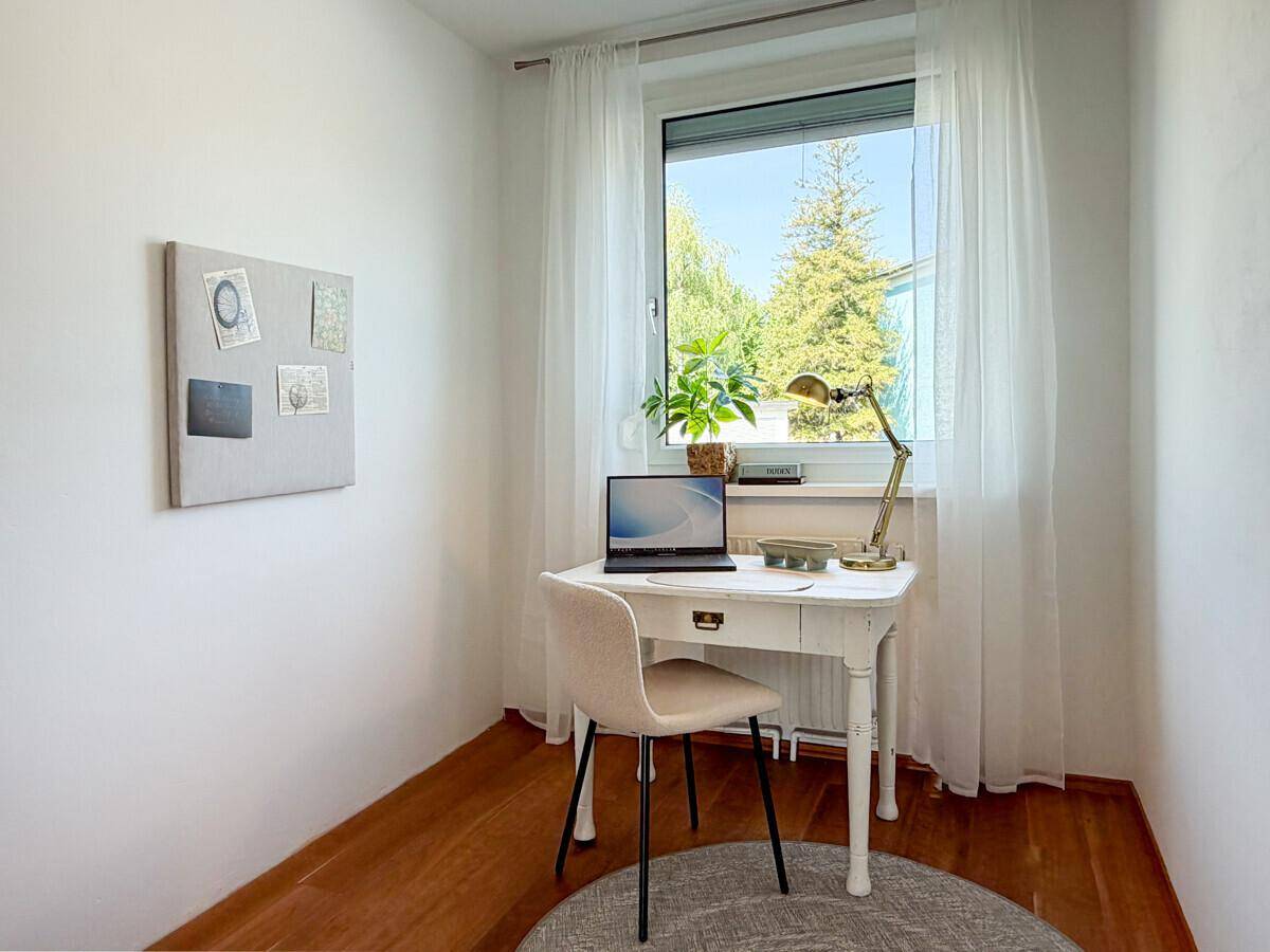 Kleines Arbeitszimmer mit Holzboden, Schreibtisch und Fenster mit Blick ins Grüne.