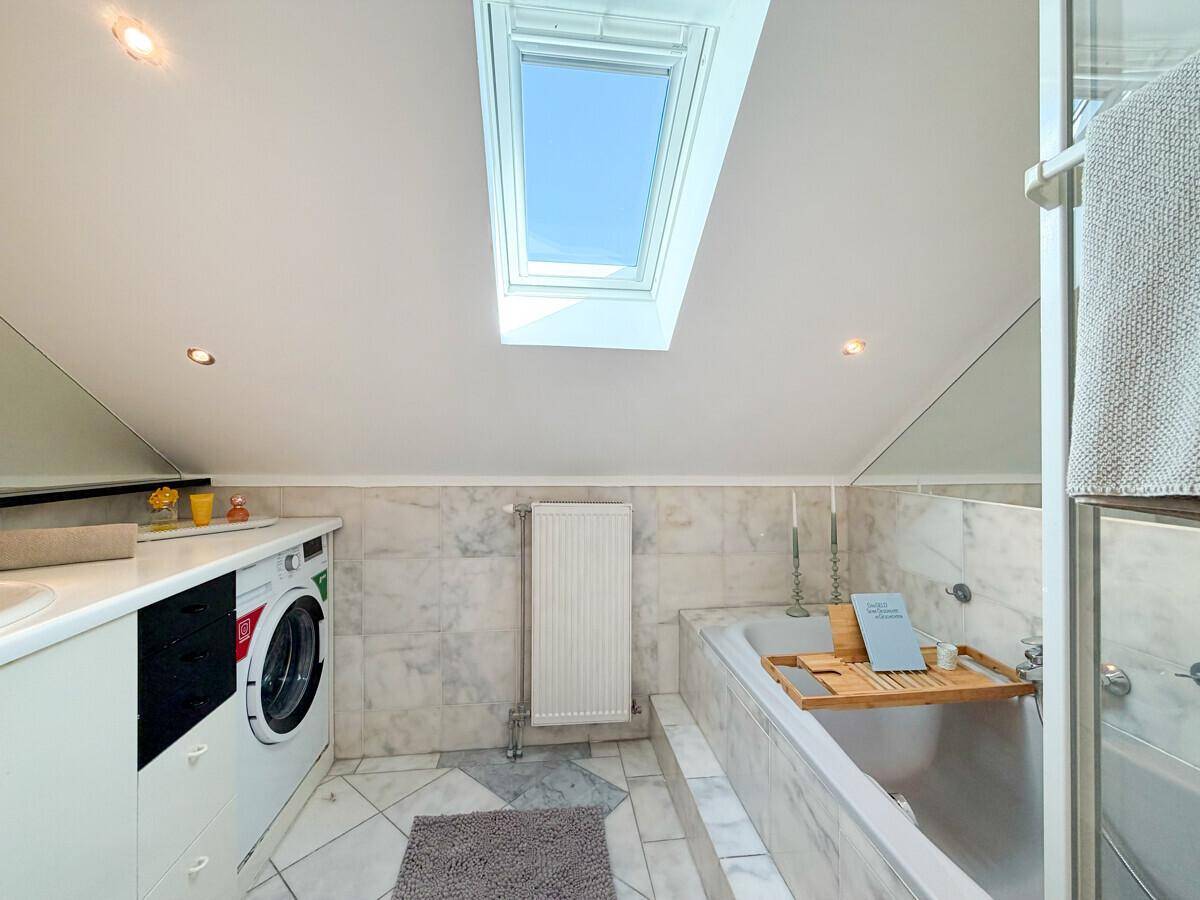 Helles Badezimmer mit Marmorfliesen, Badewanne, Waschmaschine und großem Dachfenster für viel Licht.