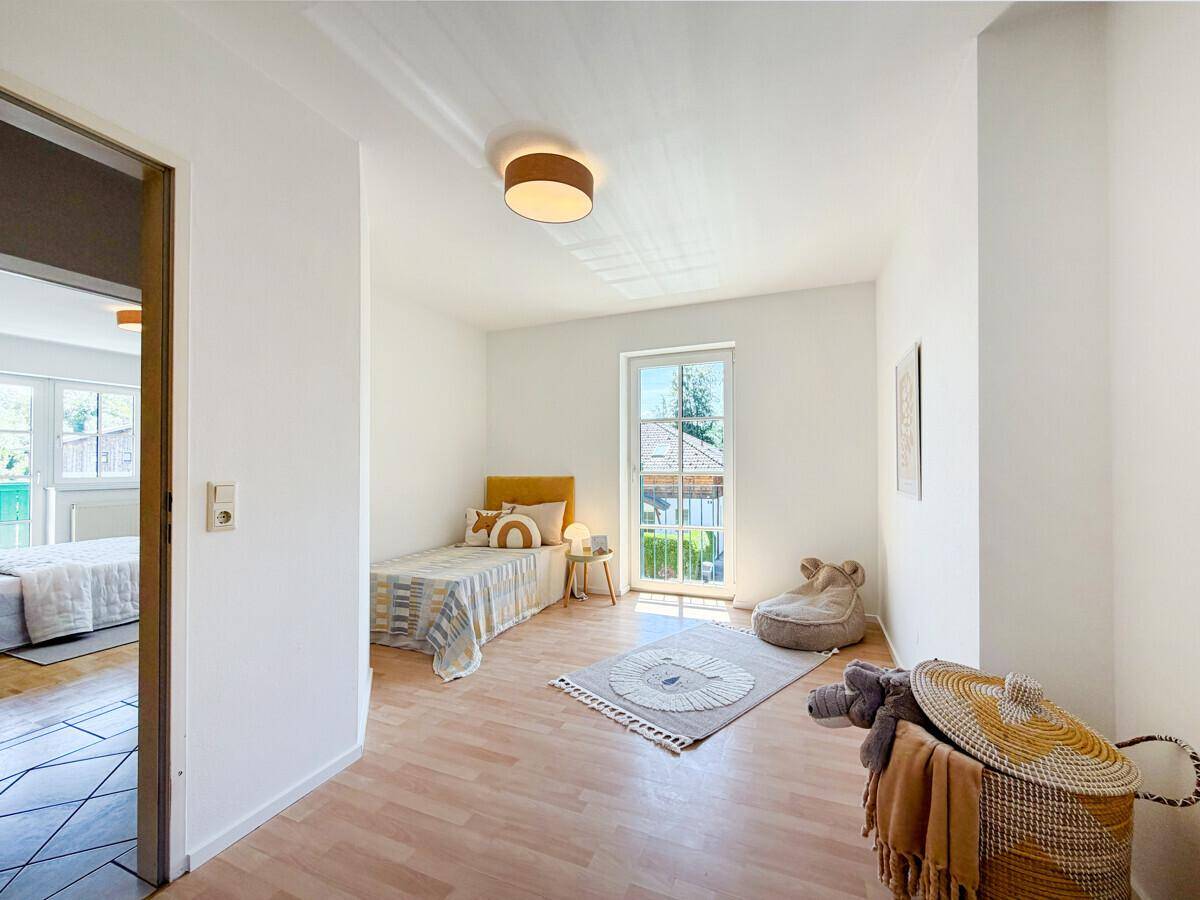 Kinderzimmer mit hellem Laminatboden, Einzelbett und Zugang zu einem französischen Balkon.