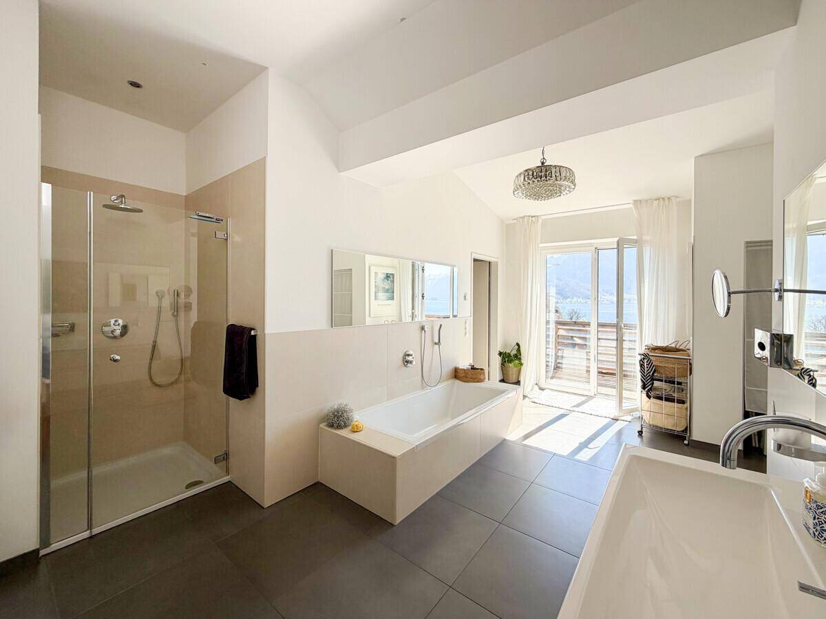 Helles, modernes Badezimmer mit Badewanne, Dusche und Zugang zu einem Balkon mit See- und Bergblick.