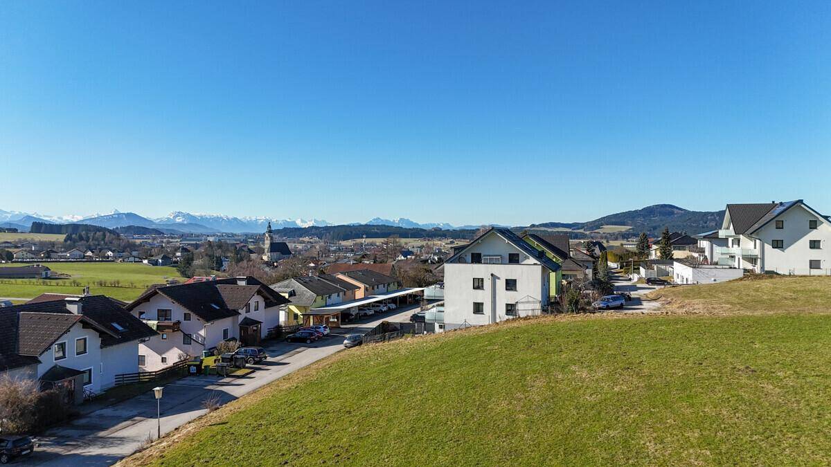 Sonnige Wohngegend mit Einfamilienhäusern und Mehrfamilienhäusern, umgeben von Natur und Bergen.