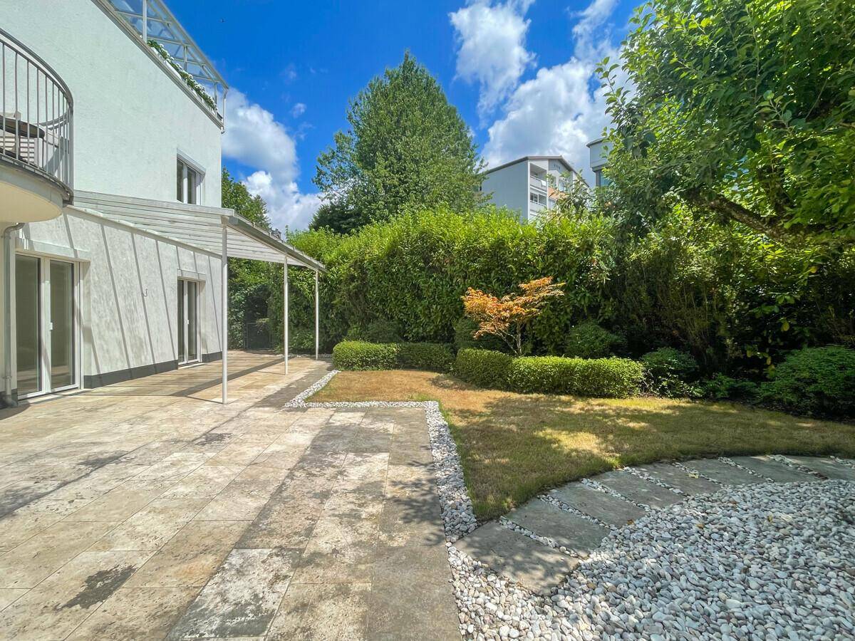 Gepflegter Gartenbereich mit Rasen, Zierpflanzen und einer großen Steinterrasse.