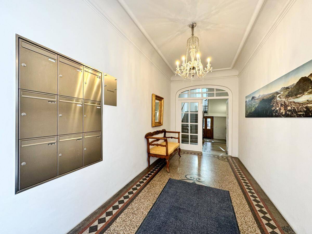 Eingangsbereich mit Briefkästen, Kronleuchter, Sitzbank und einem gemusterten Terrazzoboden.