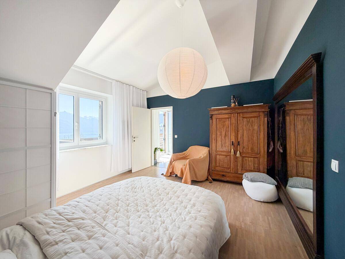 Helles Schlafzimmer mit Holzboden, blauer Akzentwand und Blick auf die umliegende Landschaft.