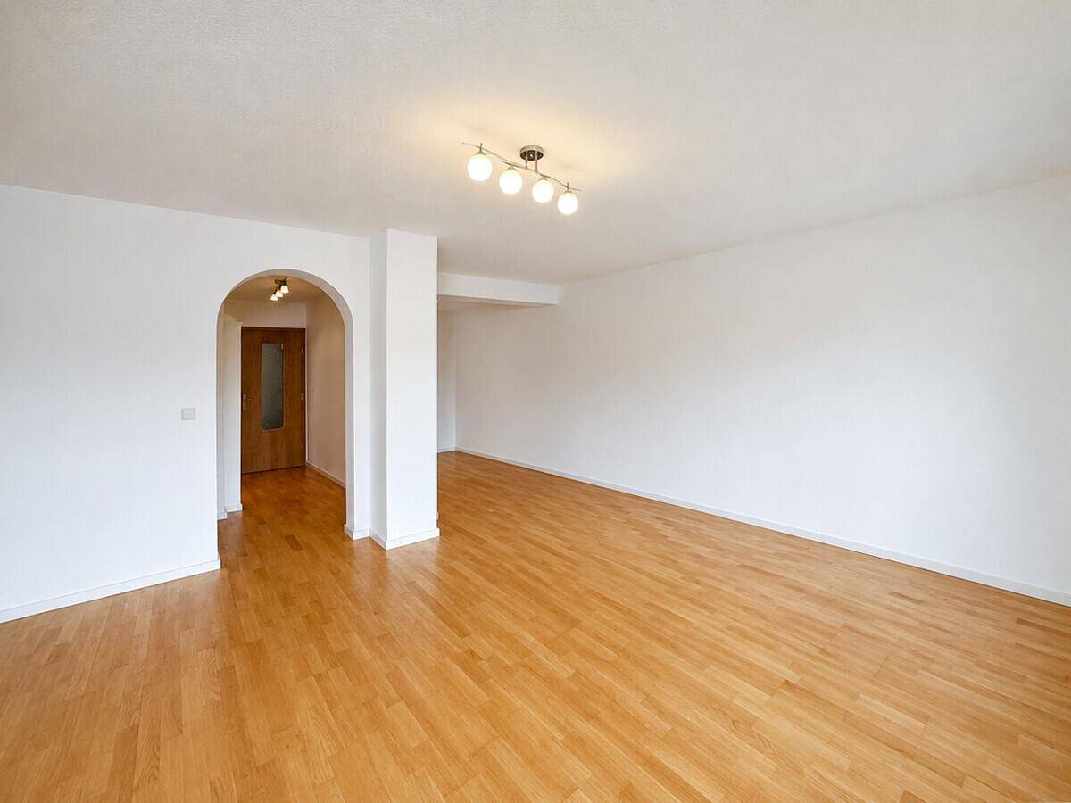 Geräumiger Wohnbereich mit Holzboden und einem Bogen zum Flur, gut beleuchtet.