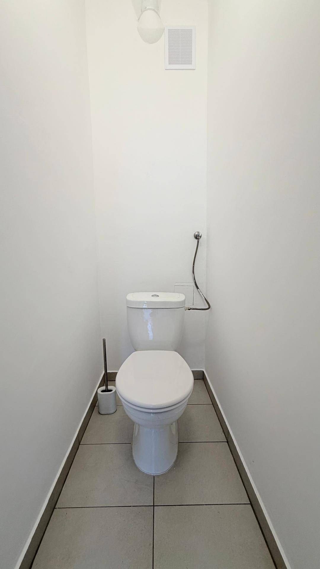 Kleines, helles WC mit weißer Toilette und grauen Bodenfliesen, funktional und sauber gestaltet.