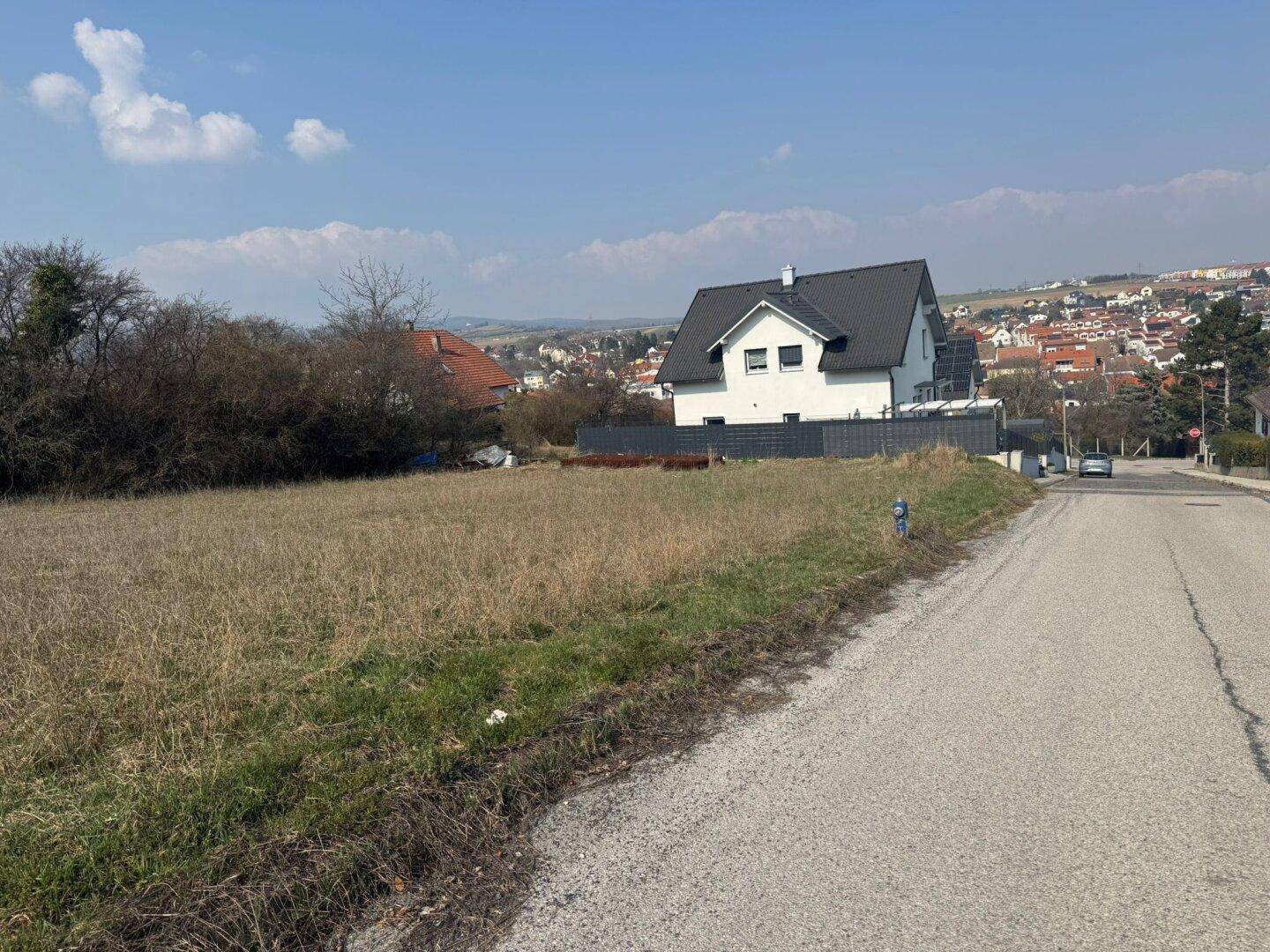 Weitläufiges unbebautes Grundstück mit Fernblick über die Stadt und angrenzende moderne Häuser.