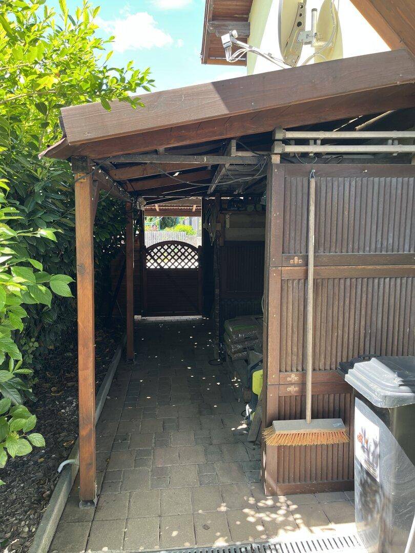 Überdachter Durchgangsbereich neben dem Haus mit Holzelementen und einem Gartentor.