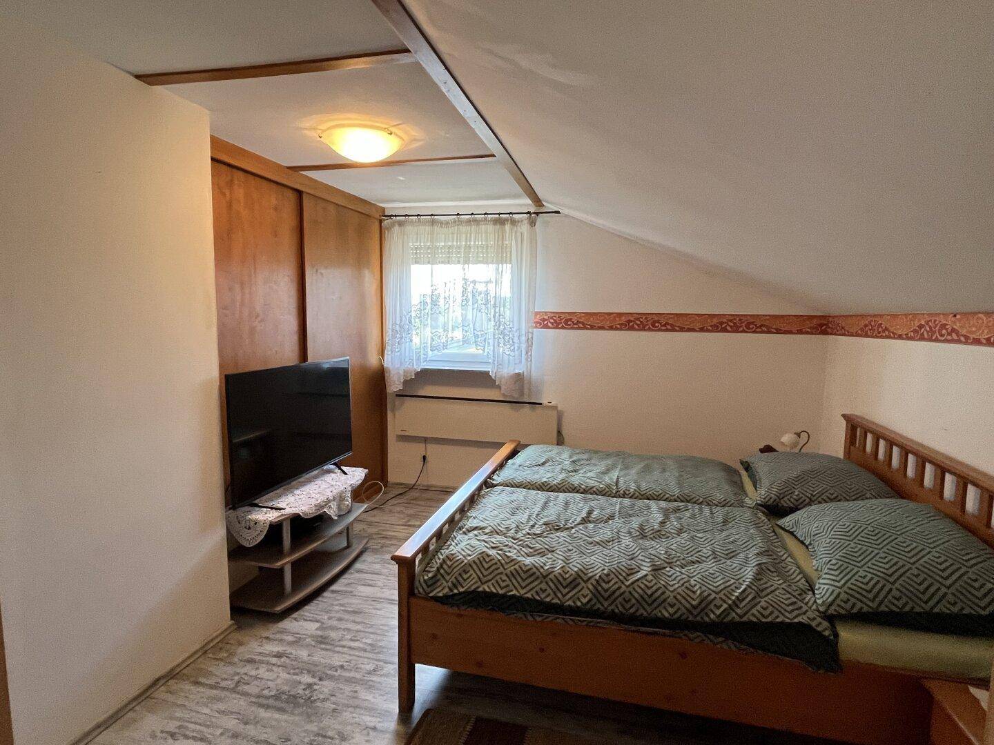 Gemütliches Schlafzimmer mit Holzbett, Fernseher und Dachschräge, ideal zum Entspannen.