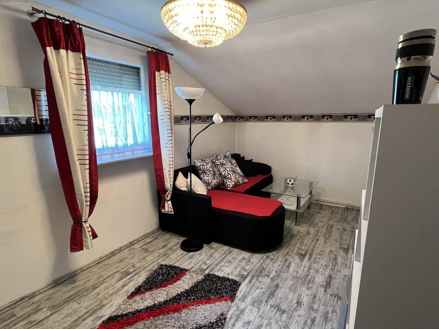 Helles Wohnzimmer mit Sofa, Stehlampe und dekorativen Elementen unter einer Dachschräge.