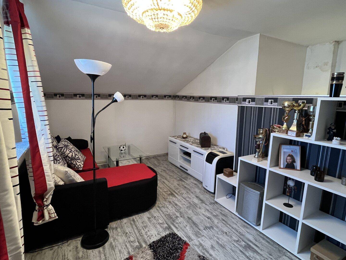Wohnzimmer mit Sofa, Regalen und dekorativen Trophäen unter einer Dachschräge.