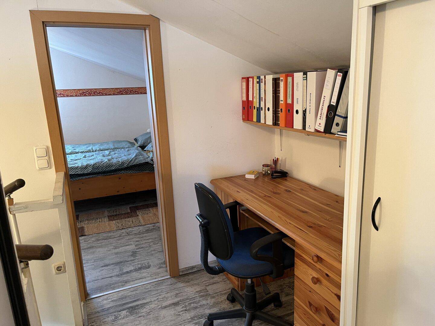 Kleiner Arbeitsbereich mit Holzschreibtisch, Bürostuhl und Regalen für Akten.