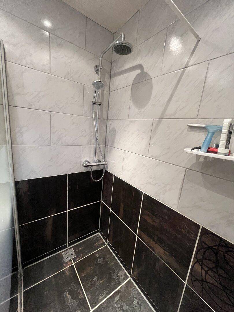 Modern geflieste Dusche mit dunklen Akzenten und Duschkopf.