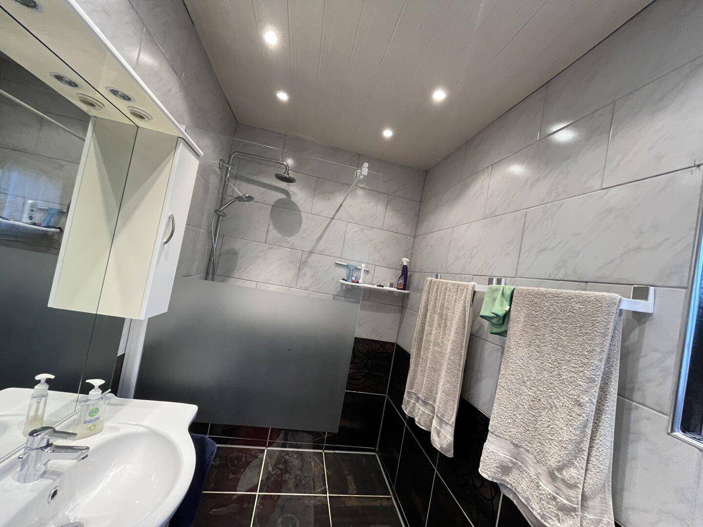 Badezimmer mit Dusche, Waschbecken und Spiegelschrank, hell gefliest.