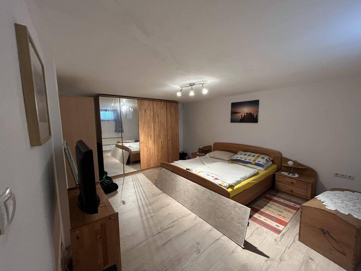 Geräumiges Schlafzimmer mit Doppelbett, großem Spiegelschrank und Holzboden.