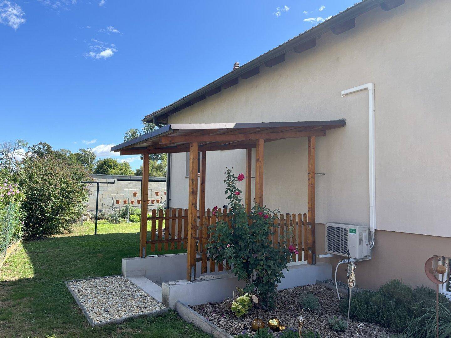 Seitenansicht des Hauses mit überdachtem Eingangsbereich, kleinem Zaun und gepflegtem Garten.