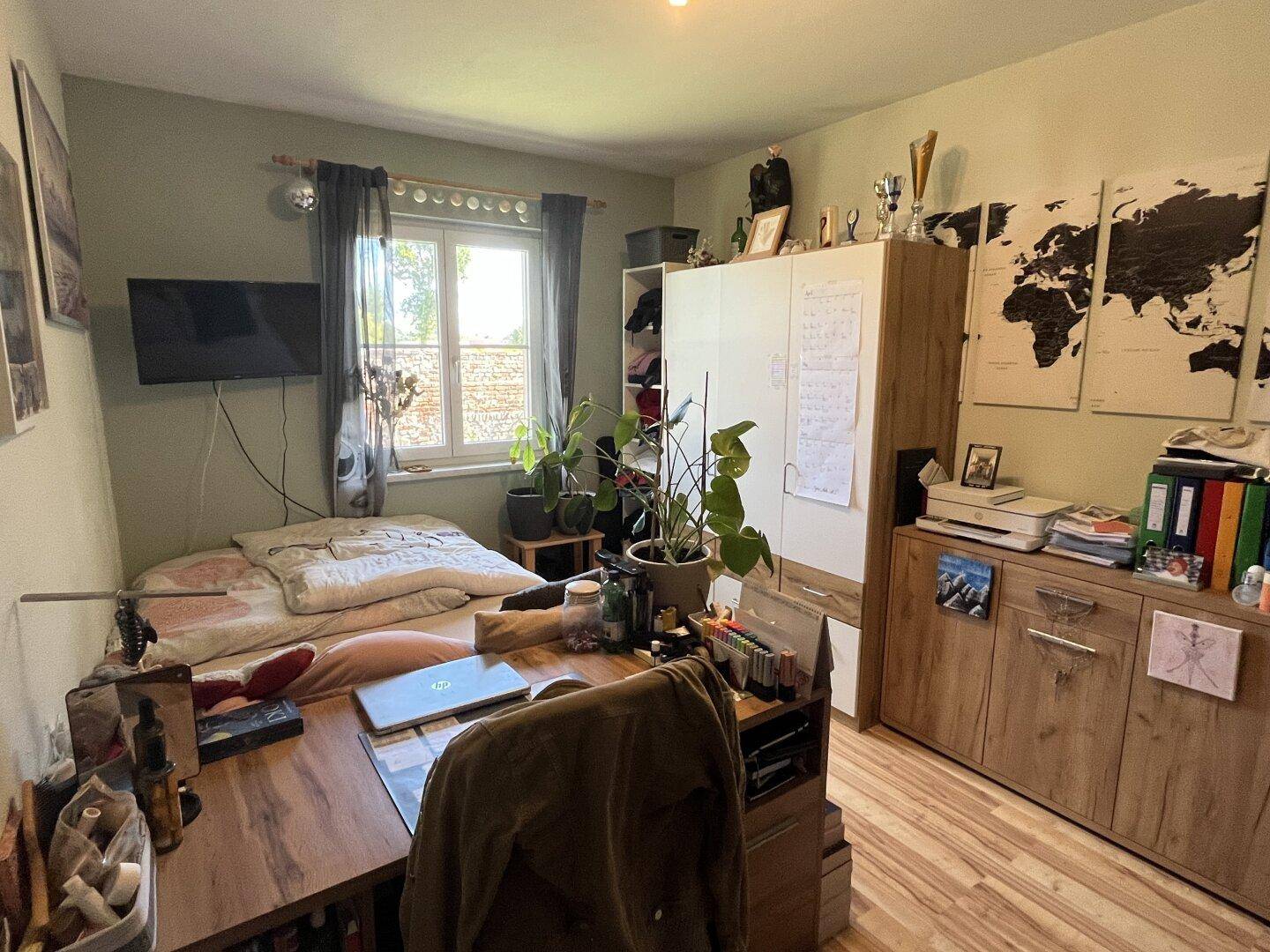 Helles Schlafzimmer mit Schreibtisch, Kleiderschrank und Blick ins Grüne.