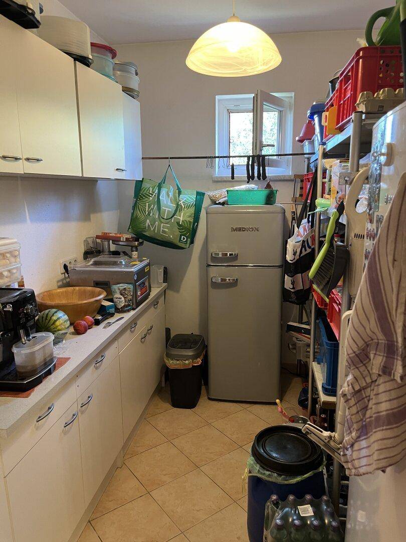 Funktionale Küche mit weißen Schränken, Kühlschrank und Fliesenboden.