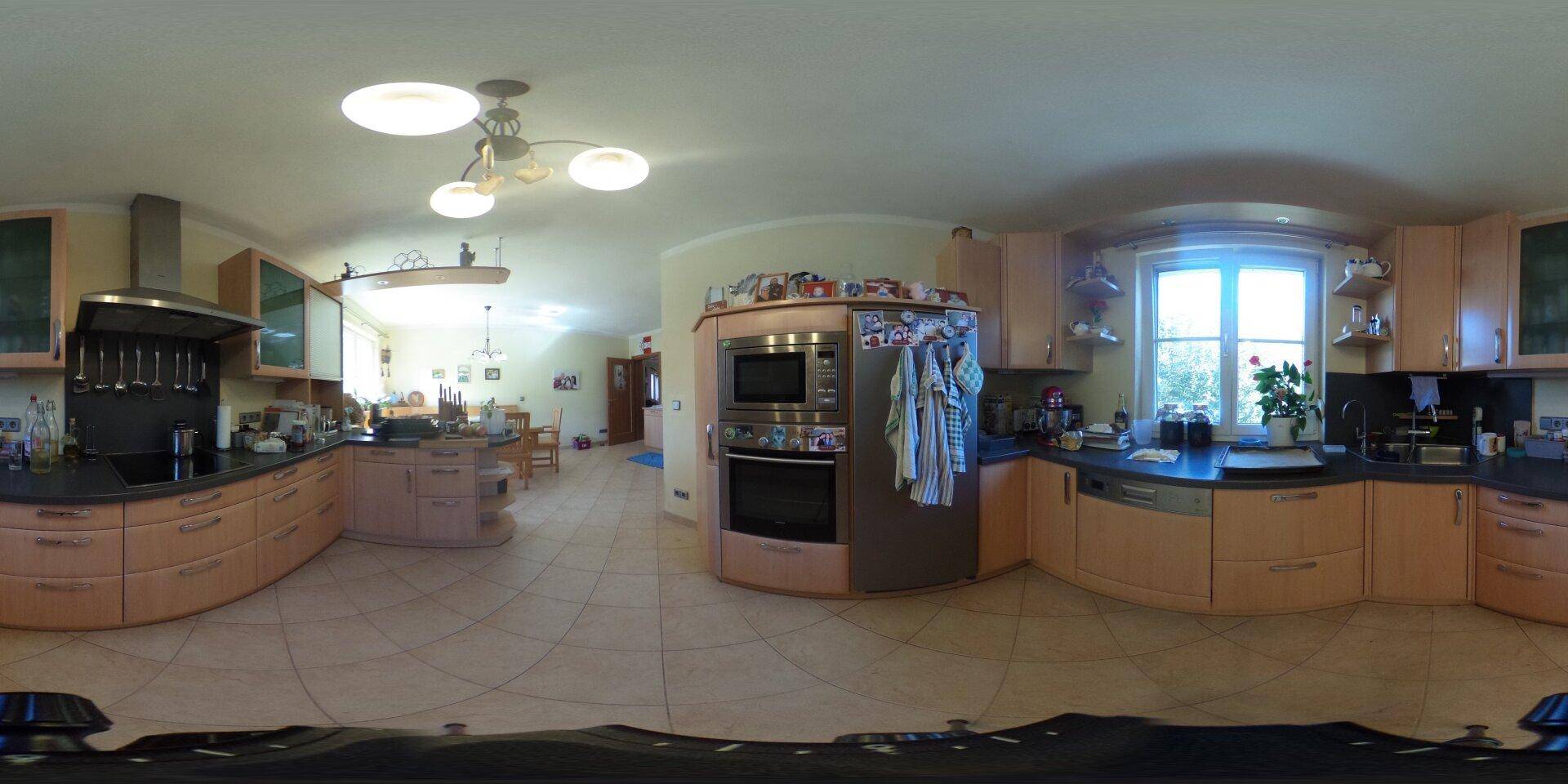 Panoramaansicht einer geräumigen Küche mit Holzschränken und Essbereich im Hintergrund.