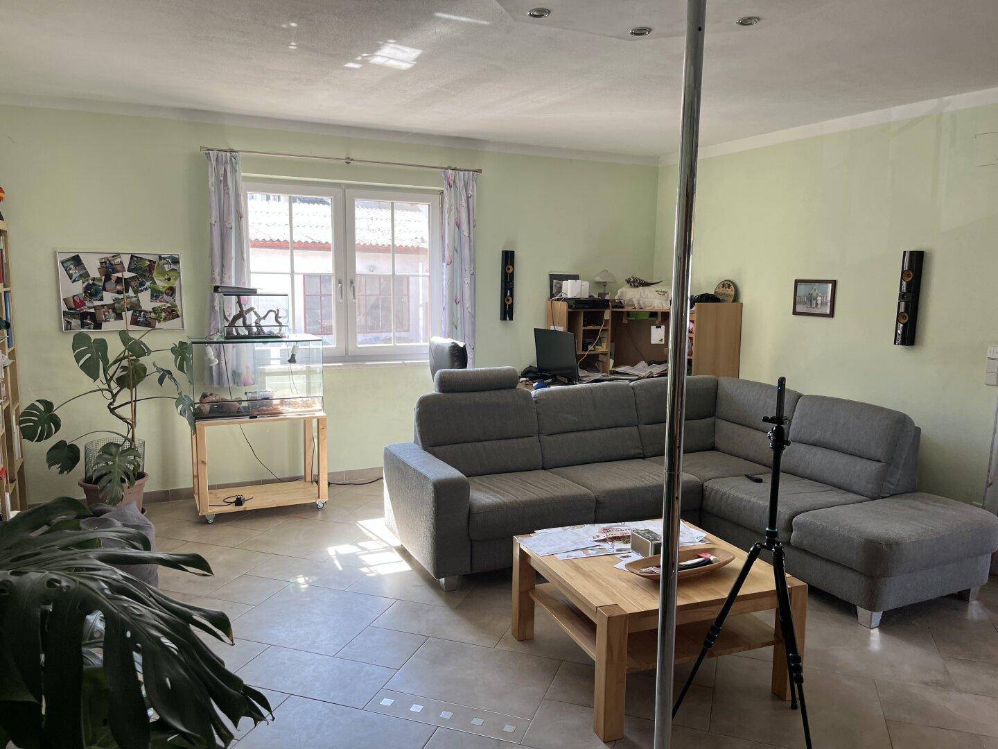Helles Wohnzimmer mit großem Sofa, Couchtisch und Fliesenboden.