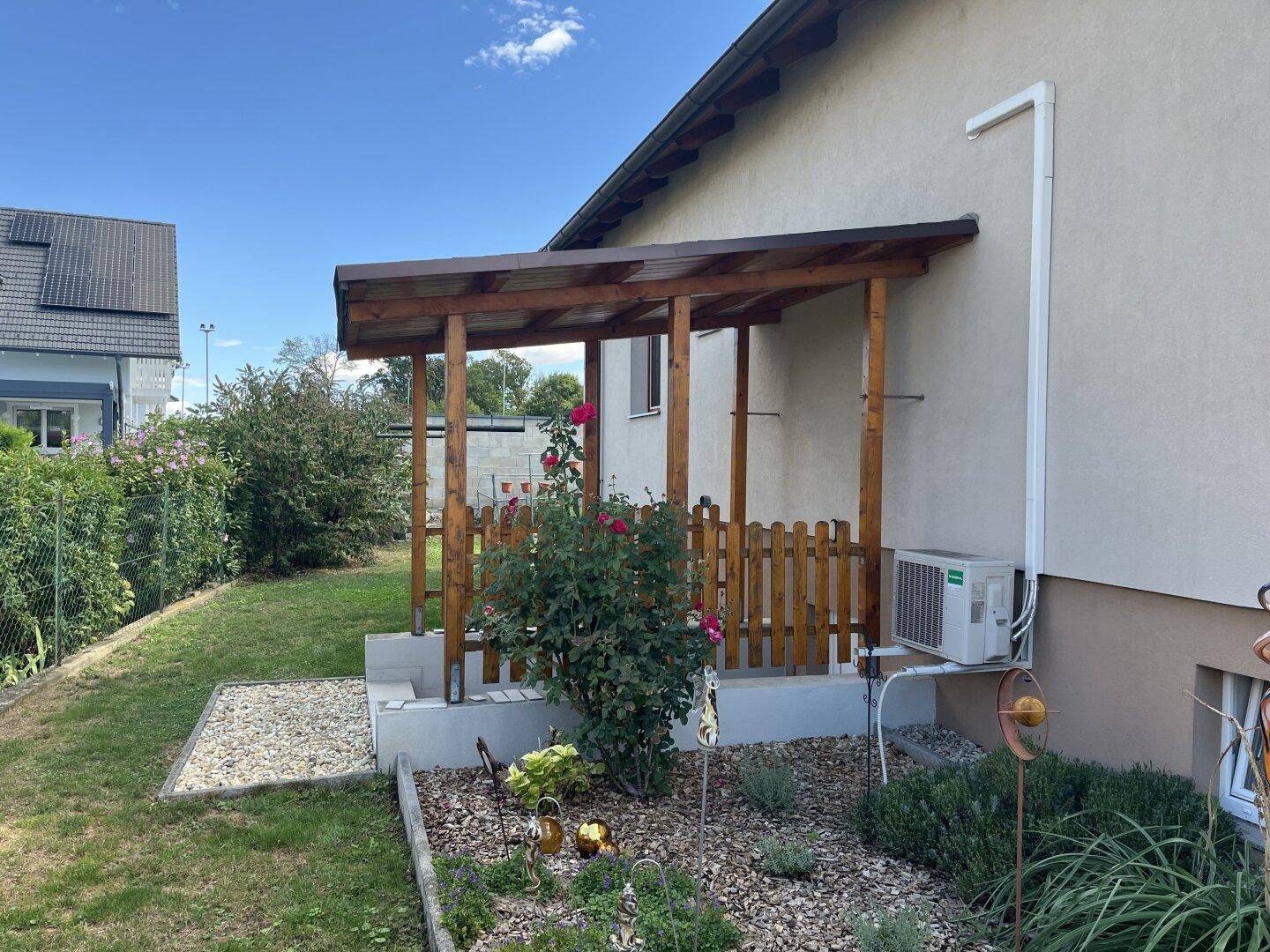Überdachte Terrasse mit Holzbalken und kleinem Gartenbereich, ideal für entspannte Stunden im Freien.
