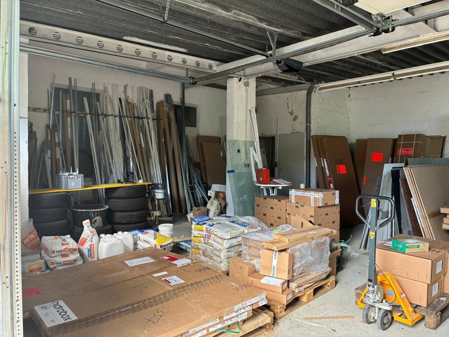 Großer Lagerraum oder Werkstatt mit Betonboden, gefüllt mit Baumaterialien und Werkzeugen.