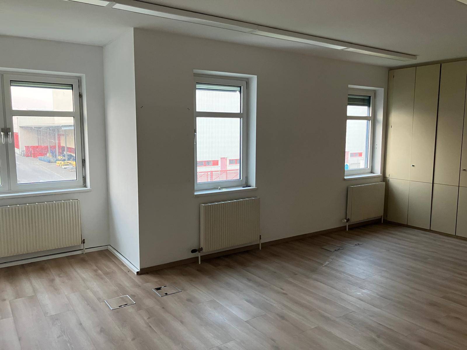 Heller Büroraum mit mehreren Fenstern, Laminatboden und integrierten Schränken, bietet vielseitige Nutzung.