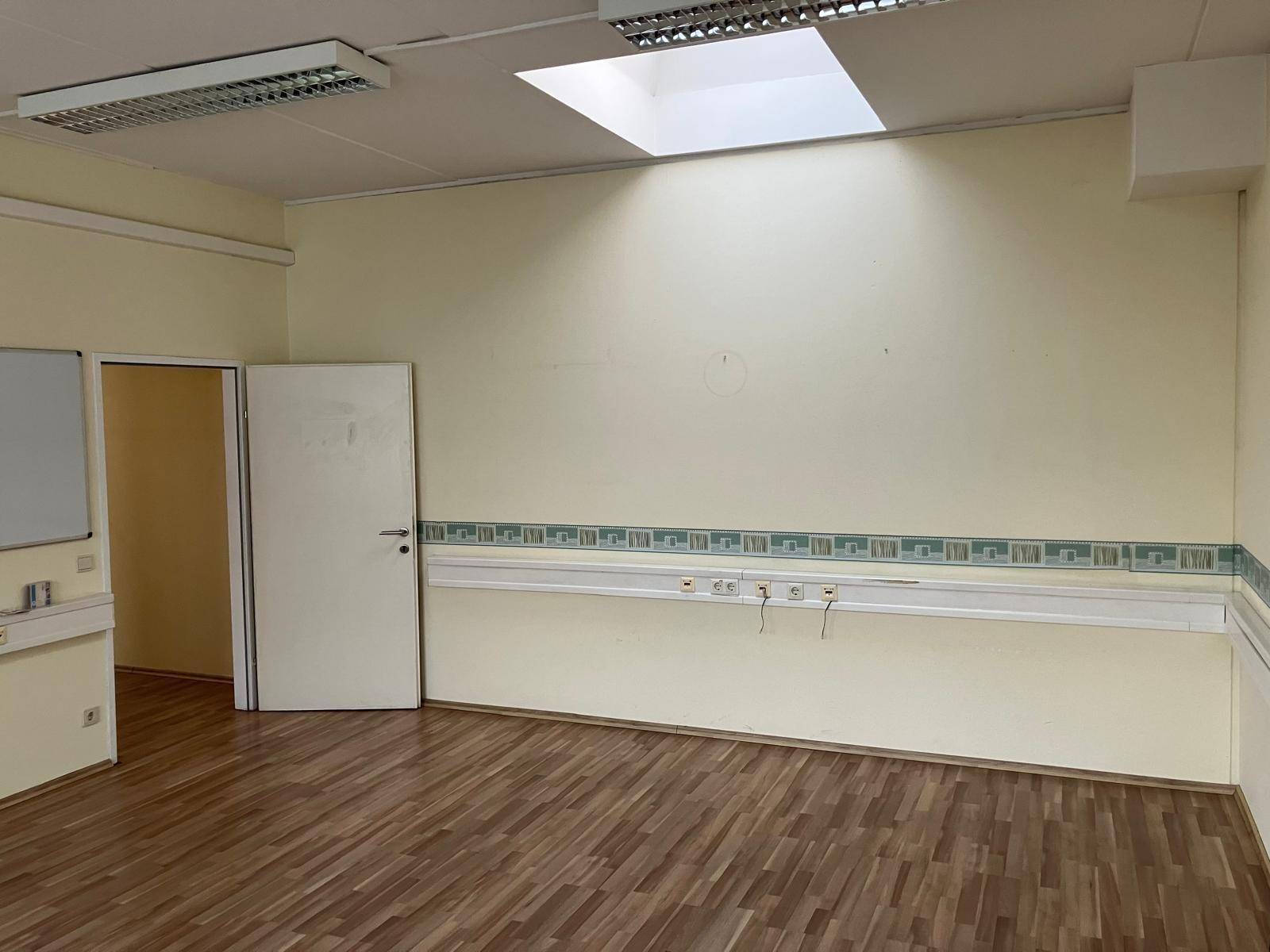 Großer Raum mit Laminatboden, Deckenleuchten und einer Tafel an der Wand, ideal für Besprechungen mit Oberlicht.