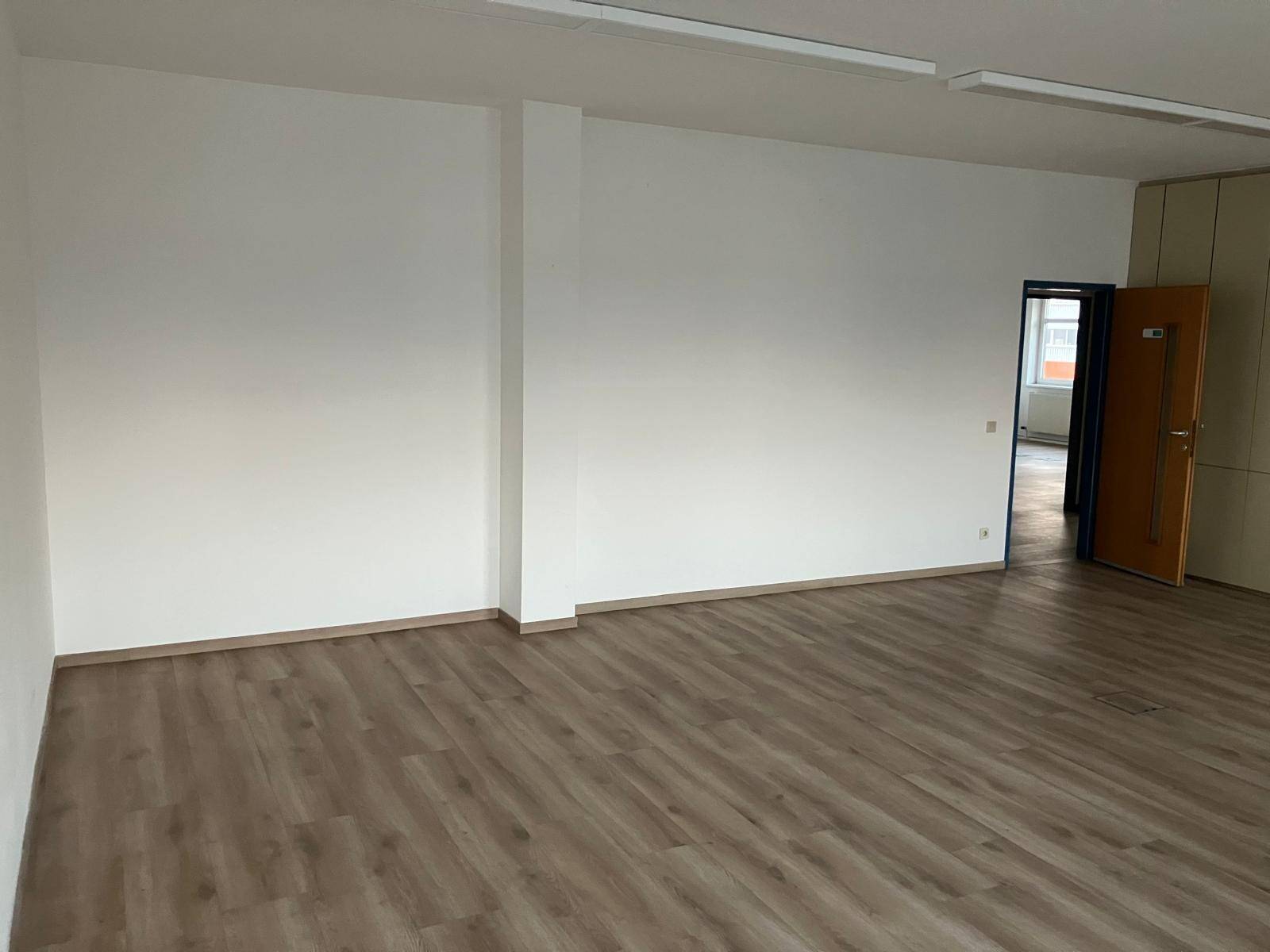 Geräumiger, leerer Büroraum mit weißen Wänden und Laminatboden, ideal für verschiedene Nutzungen.