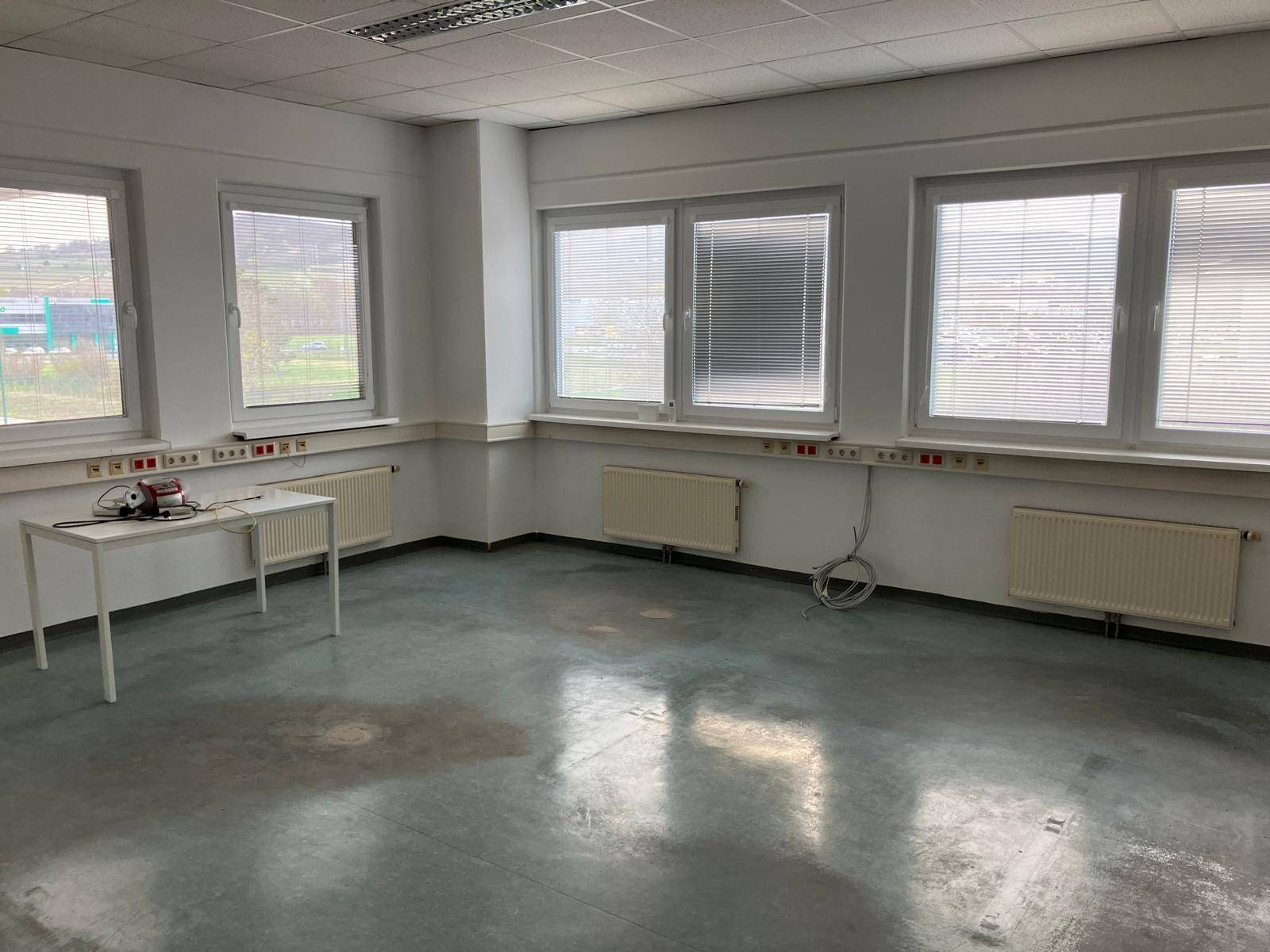 Helles Büro mit mehreren Fenstern, Heizkörpern und einem robusten Bodenbelag, unmöbliert und funktional.