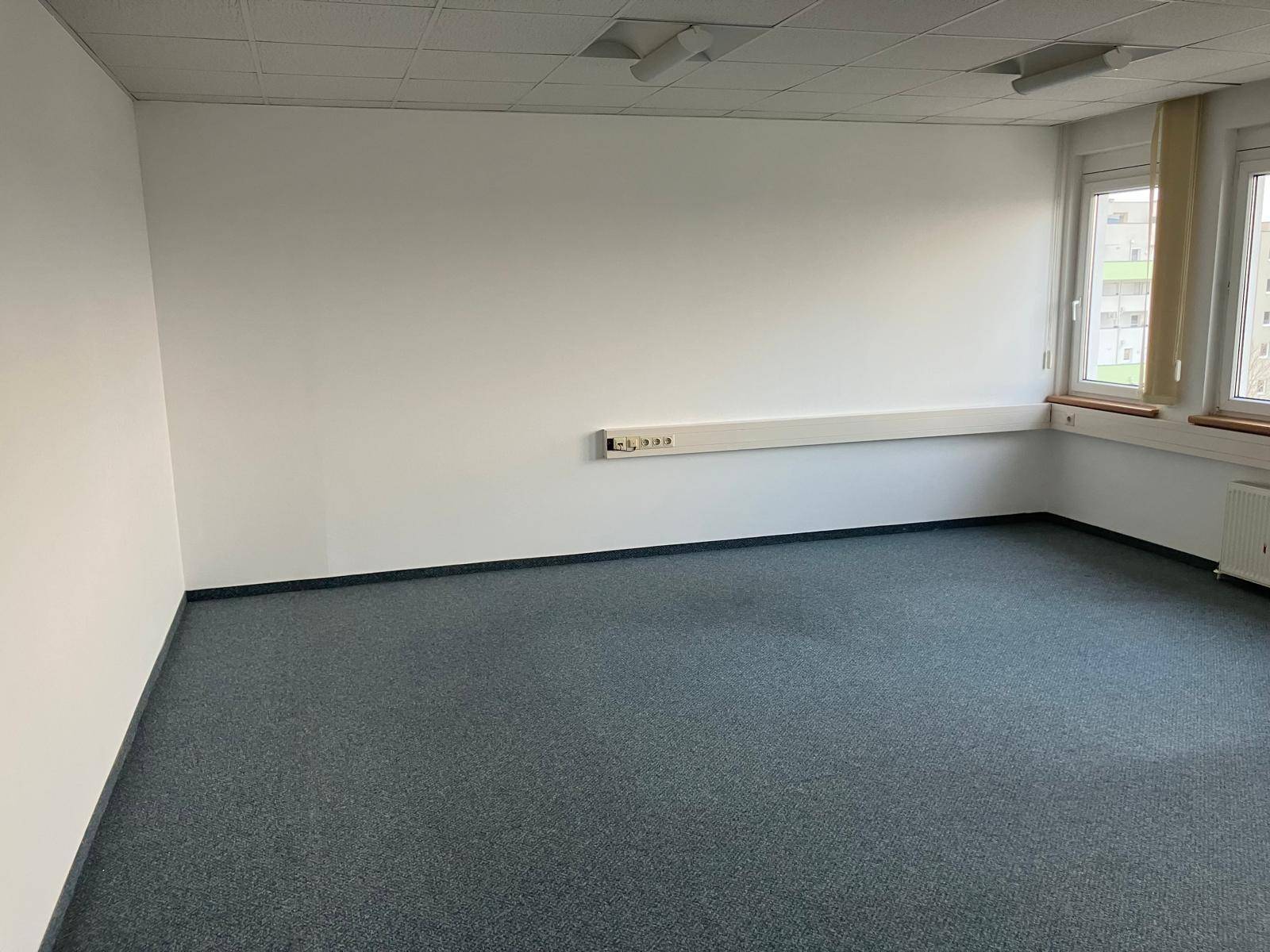 Büroraum mit Teppichboden, weißen Wänden und einer langen Steckdosenleiste.