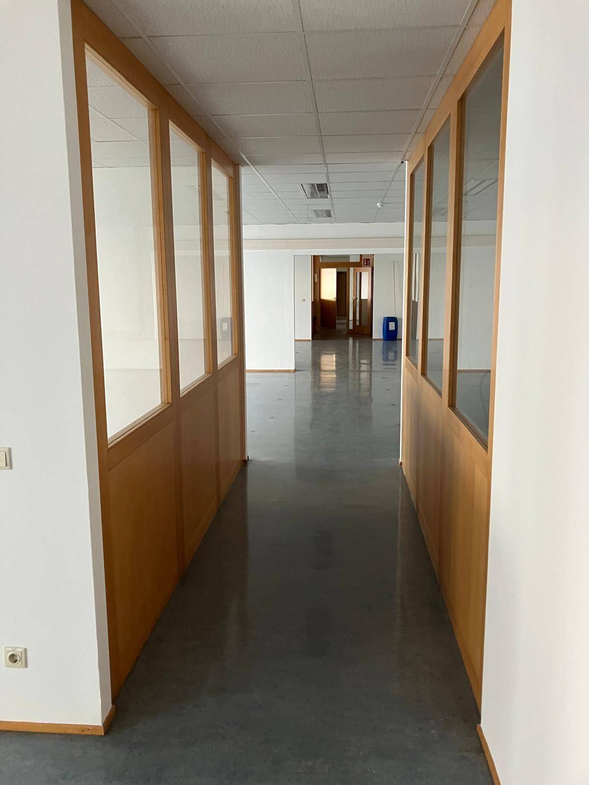 Langer Flur mit beidseitigen Holz-Glas-Trennwänden, die zu den Büros führen.