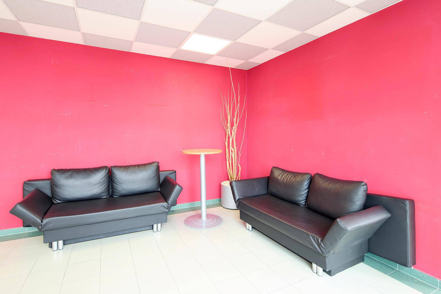 Sitzbereich mit zwei schwarzen Sofas, einem Stehtisch und einer auffälligen roten Wandgestaltung.
