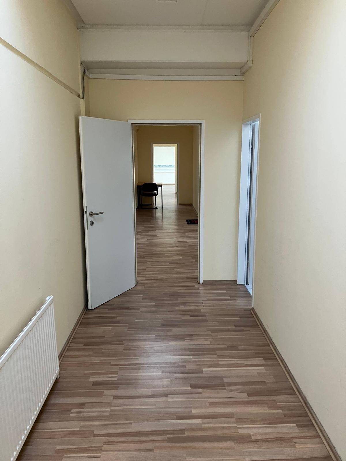 Heller Flur mit Laminatboden und Heizkörper, der zu weiteren Räumen führt und Tageslicht empfängt.