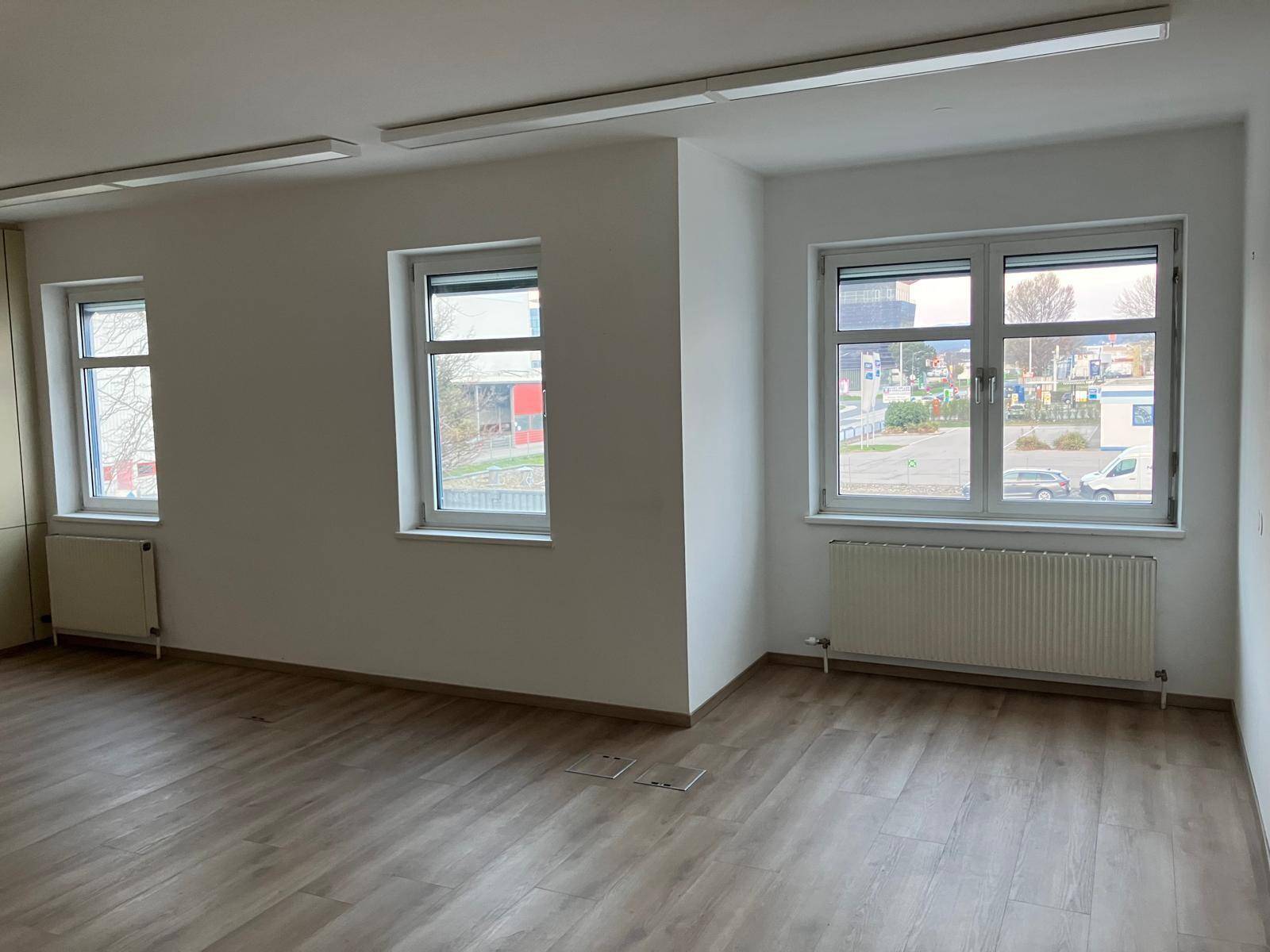 Großer, heller Büroraum mit mehreren Fenstern, Laminatboden und Heizkörpern, ideal für Arbeitsbereiche.