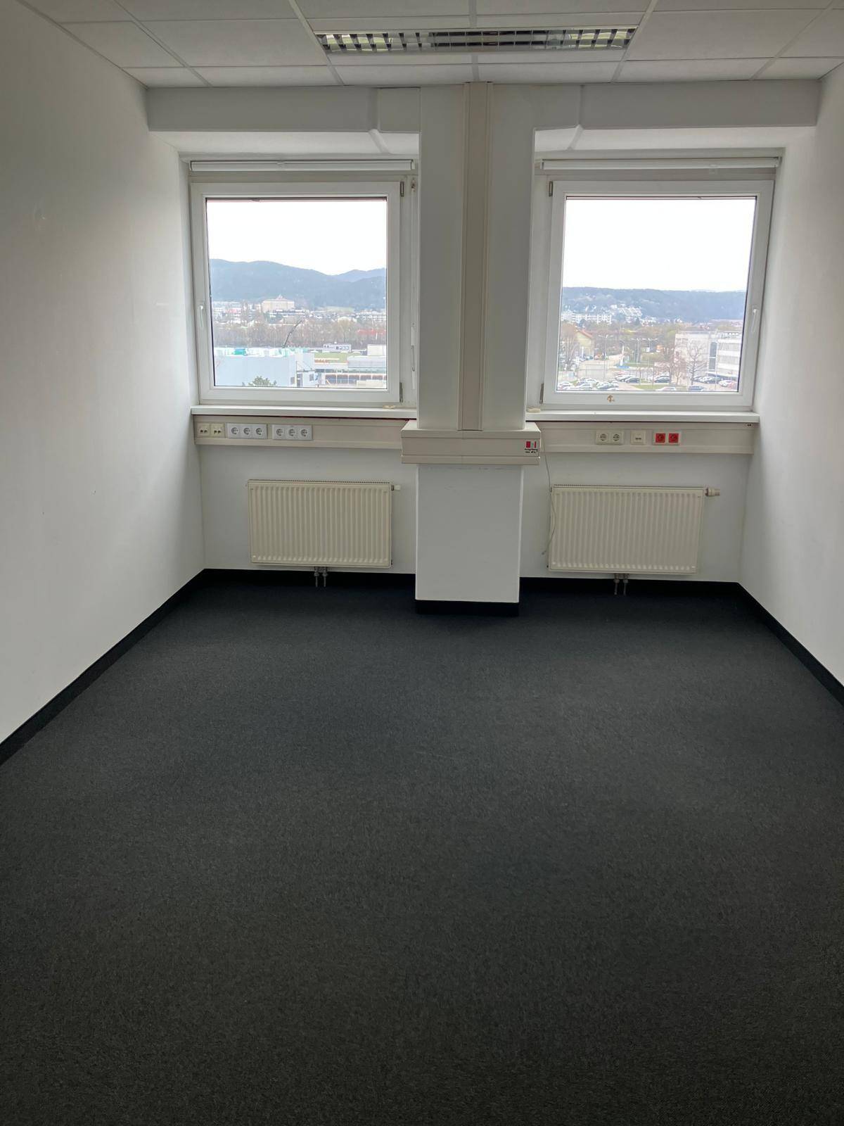 Helles Büro mit zwei großen Fenstern, die einen weiten Blick auf die Stadt und die Berge bieten.