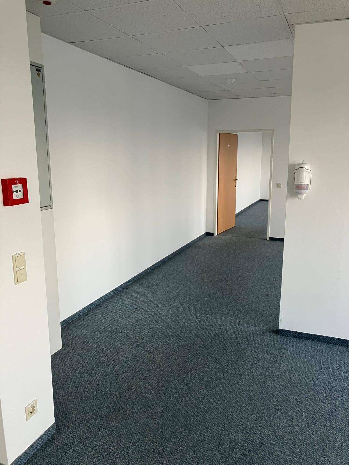 Langer Bürogang mit Teppichboden und weißen Wänden, führt zu weiteren Büros.