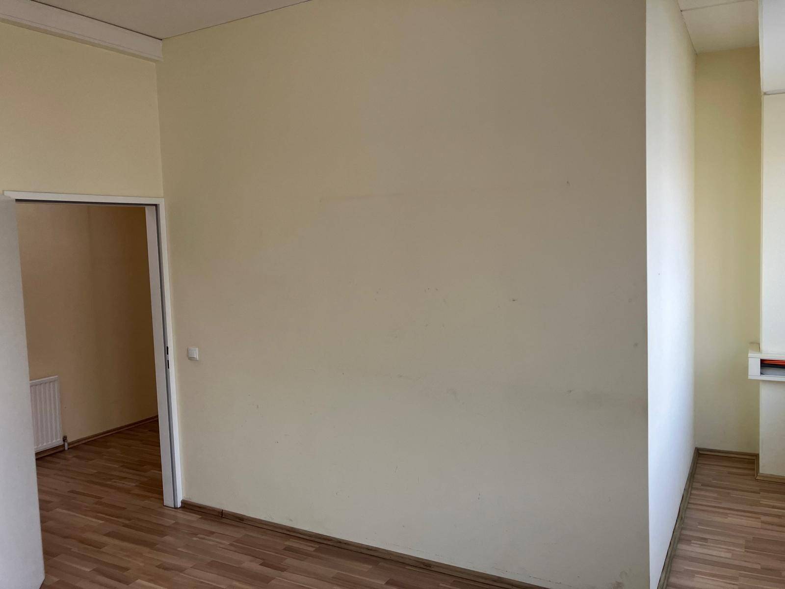 Leerer Raum mit hellen Wänden und Laminatboden, der durch eine offene Tür zugänglich ist.