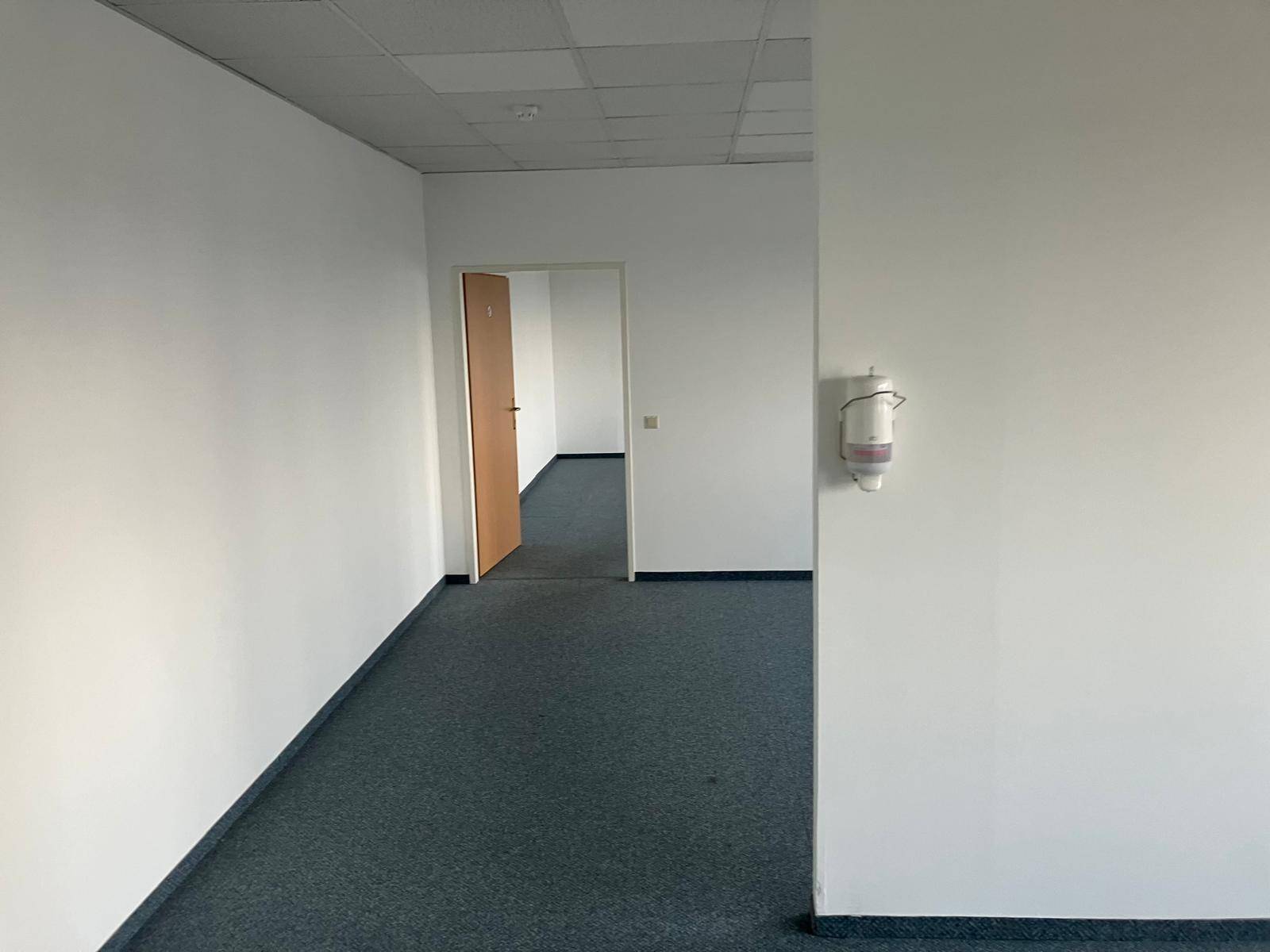 Heller Bürogang mit Teppichboden und weißen Wänden, führt zu weiteren Räumen.