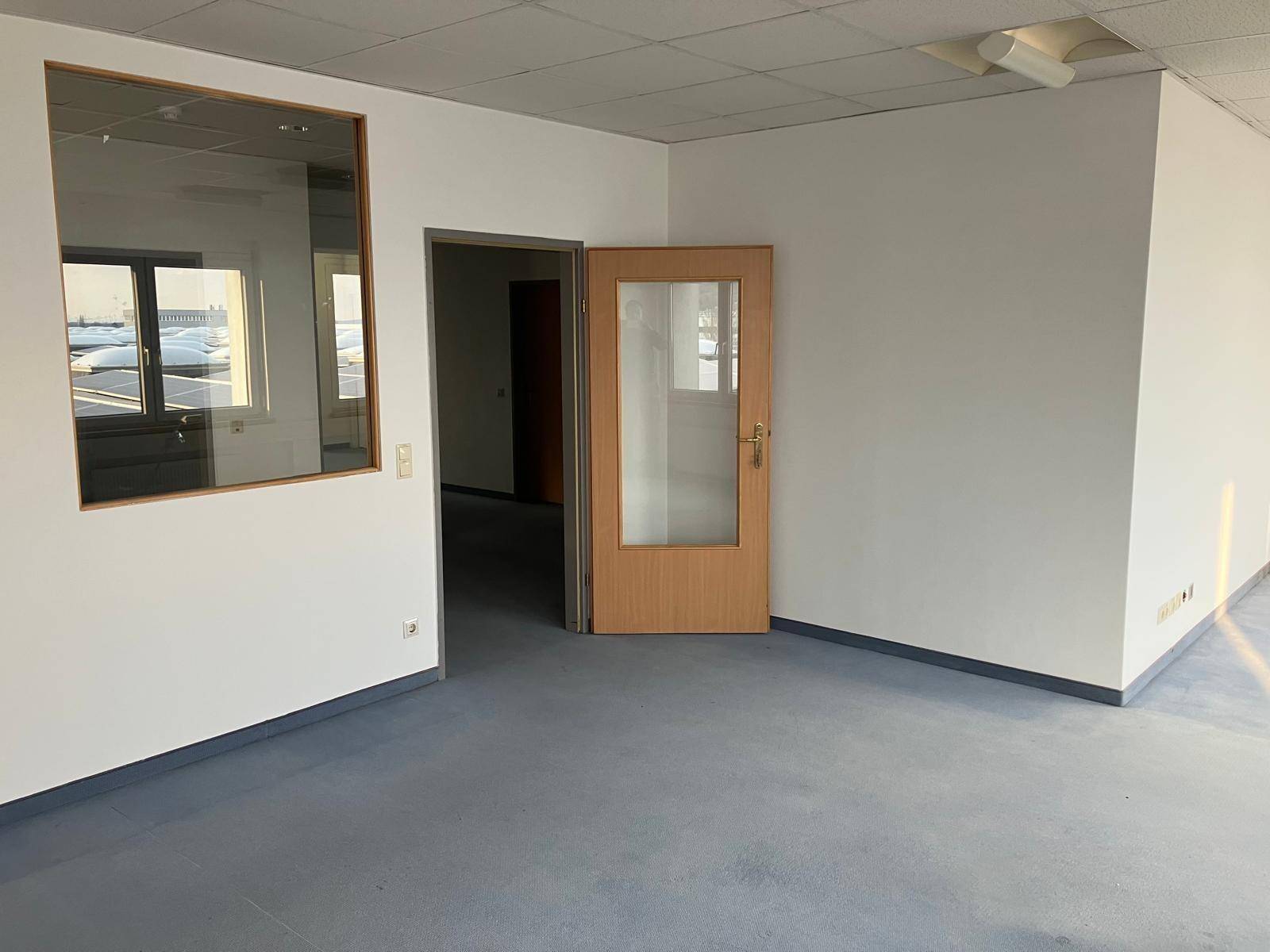 Leerer Bürobereich mit einer Glaswand, Holztür und hellem Vinylboden, der vielseitige Nutzungsmöglichkeiten bietet.