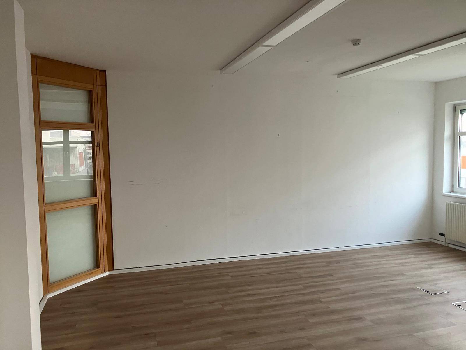 Heller Büroraum mit einer markanten, gebogenen Holztür und Laminatboden, bietet vielseitige Nutzungsmöglichkeiten.