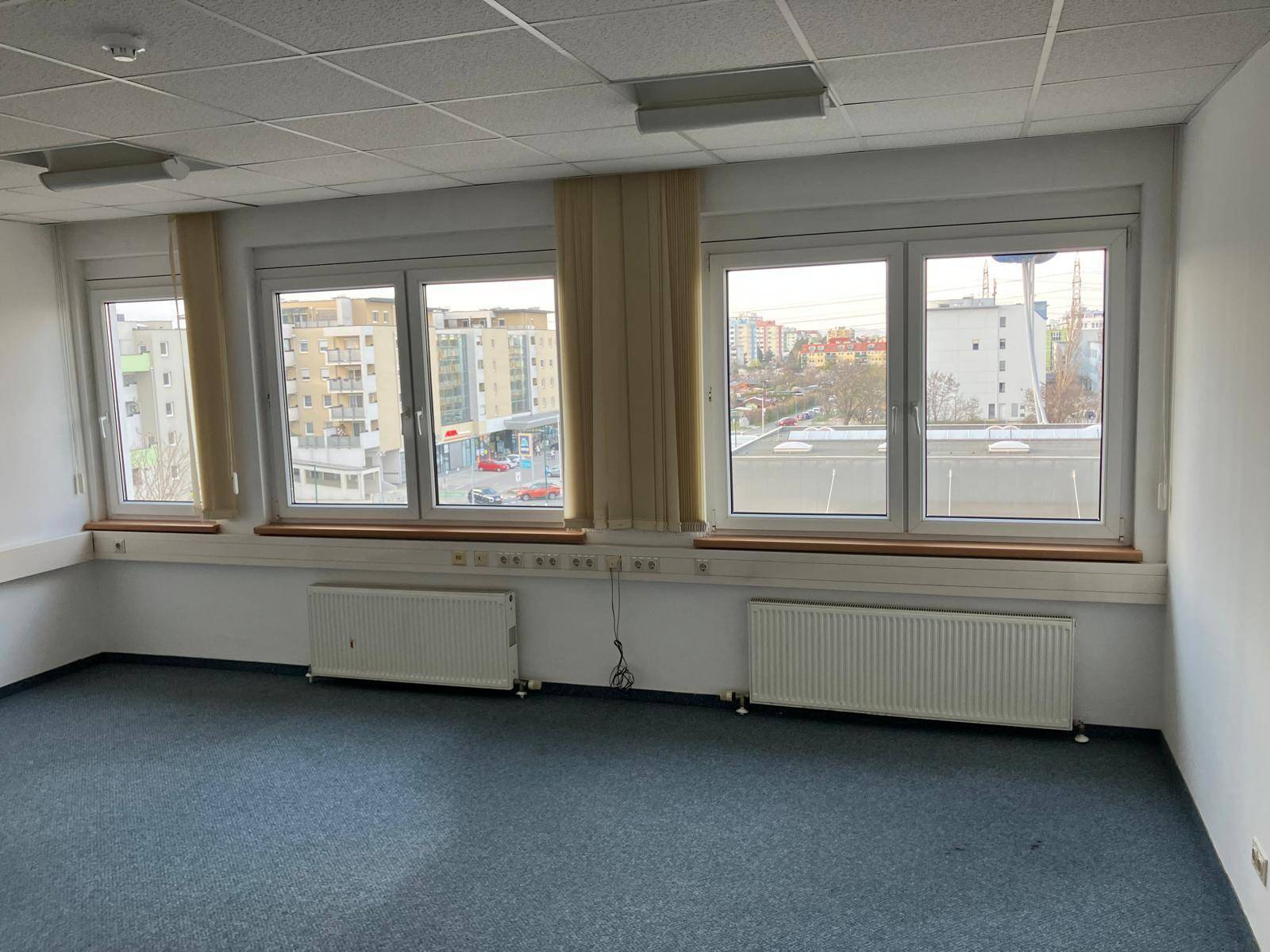 Geräumiger Büroraum mit Teppichboden, Heizkörpern und mehreren Fenstern mit Stadtblick.