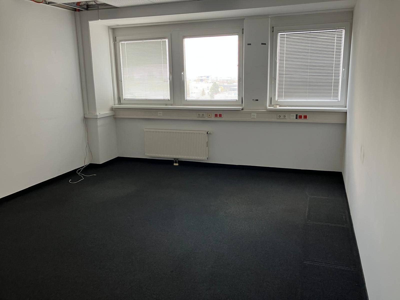 Helles Büro mit drei Fenstern, Heizkörpern und dunklem Teppichboden, ideal für Arbeitsplätze.