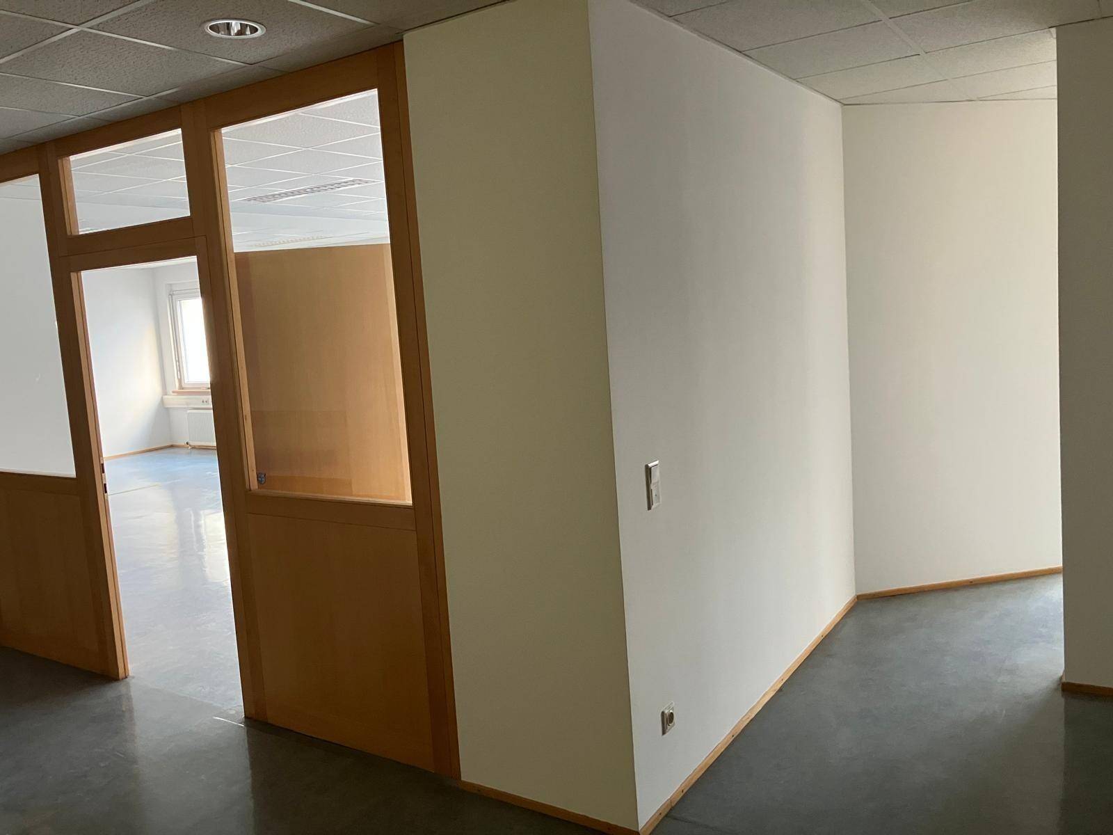 Büroecke mit weißer Wand und Holz-Glas-Trennwänden, die den Raum strukturieren.