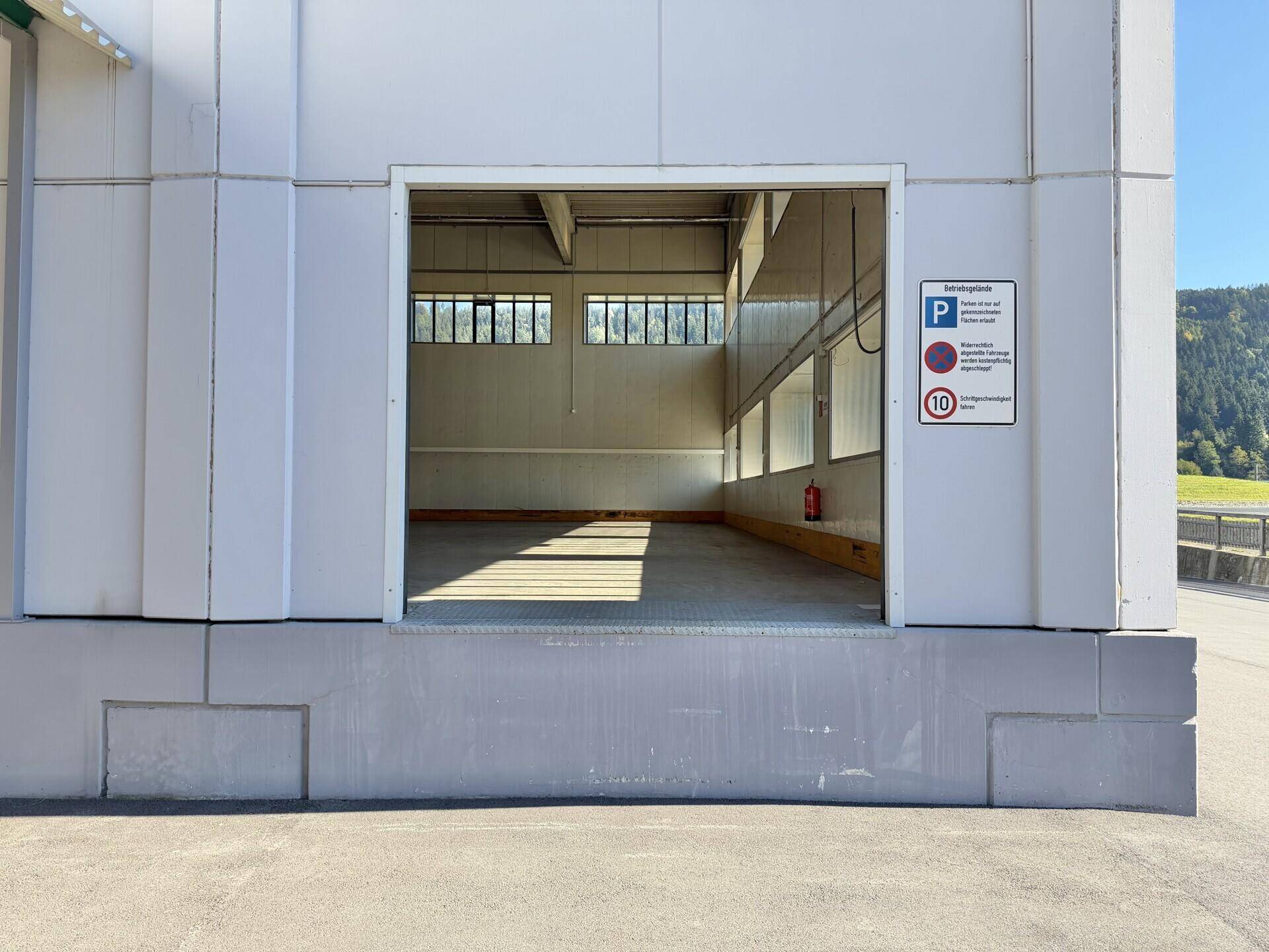 Eingangsbereich einer Lagerhalle mit Blick ins Innere und einem Hinweisschild für Parkplätze.