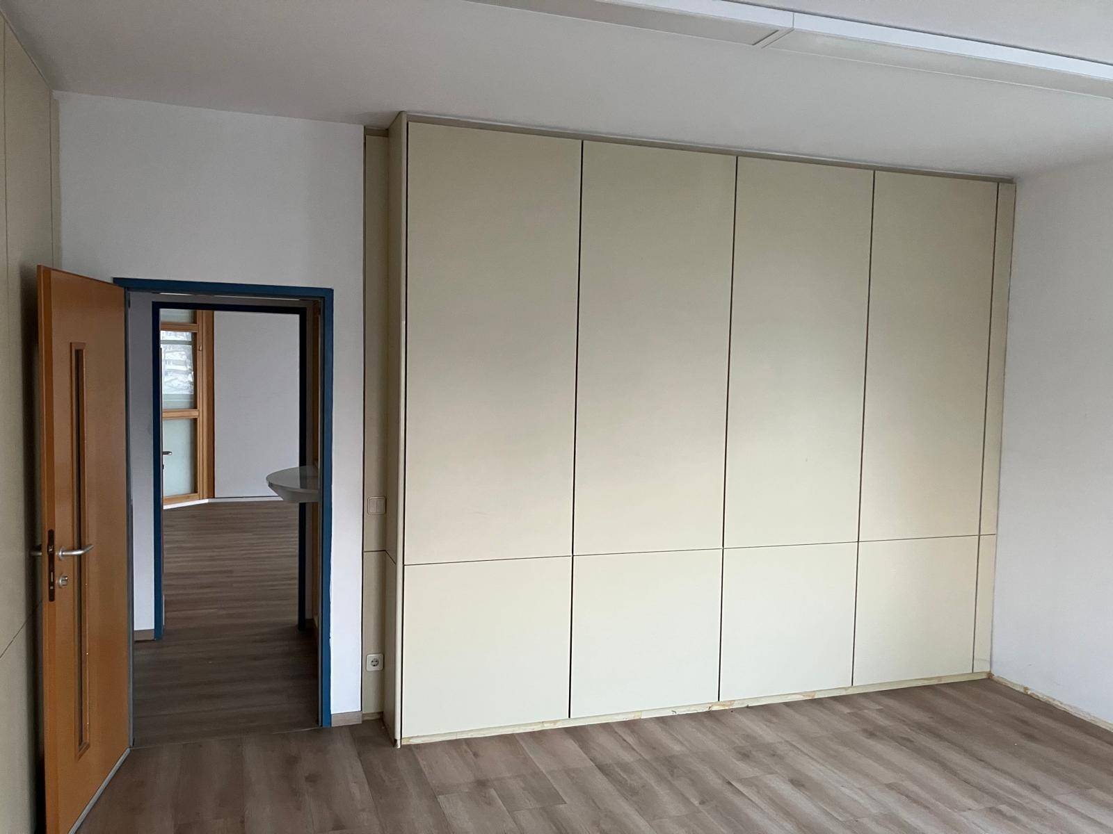 Detailansicht eines Büroraums mit raumhohen Einbauschränken und einem Durchgang zu einem weiteren Bereich.