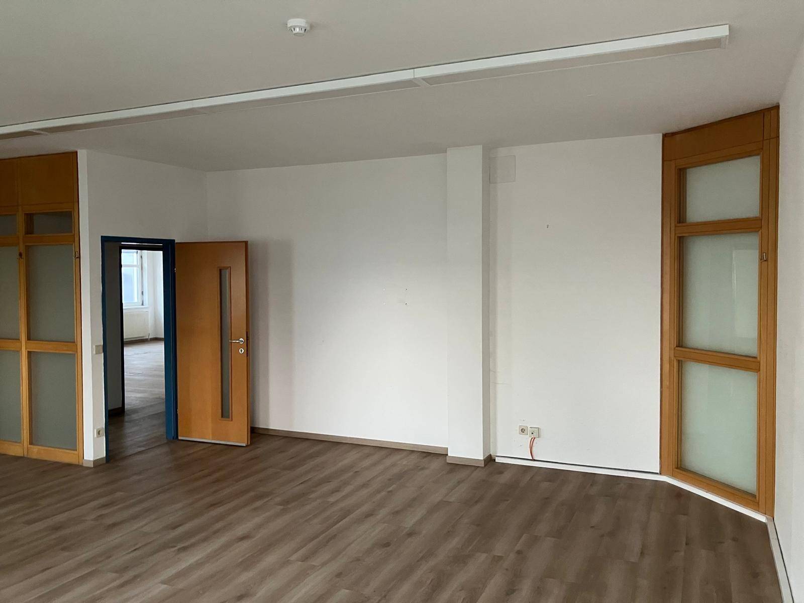 Büroraum mit einer markanten Holztür und einem weiteren Durchgang, bietet eine flexible Raumgestaltung.