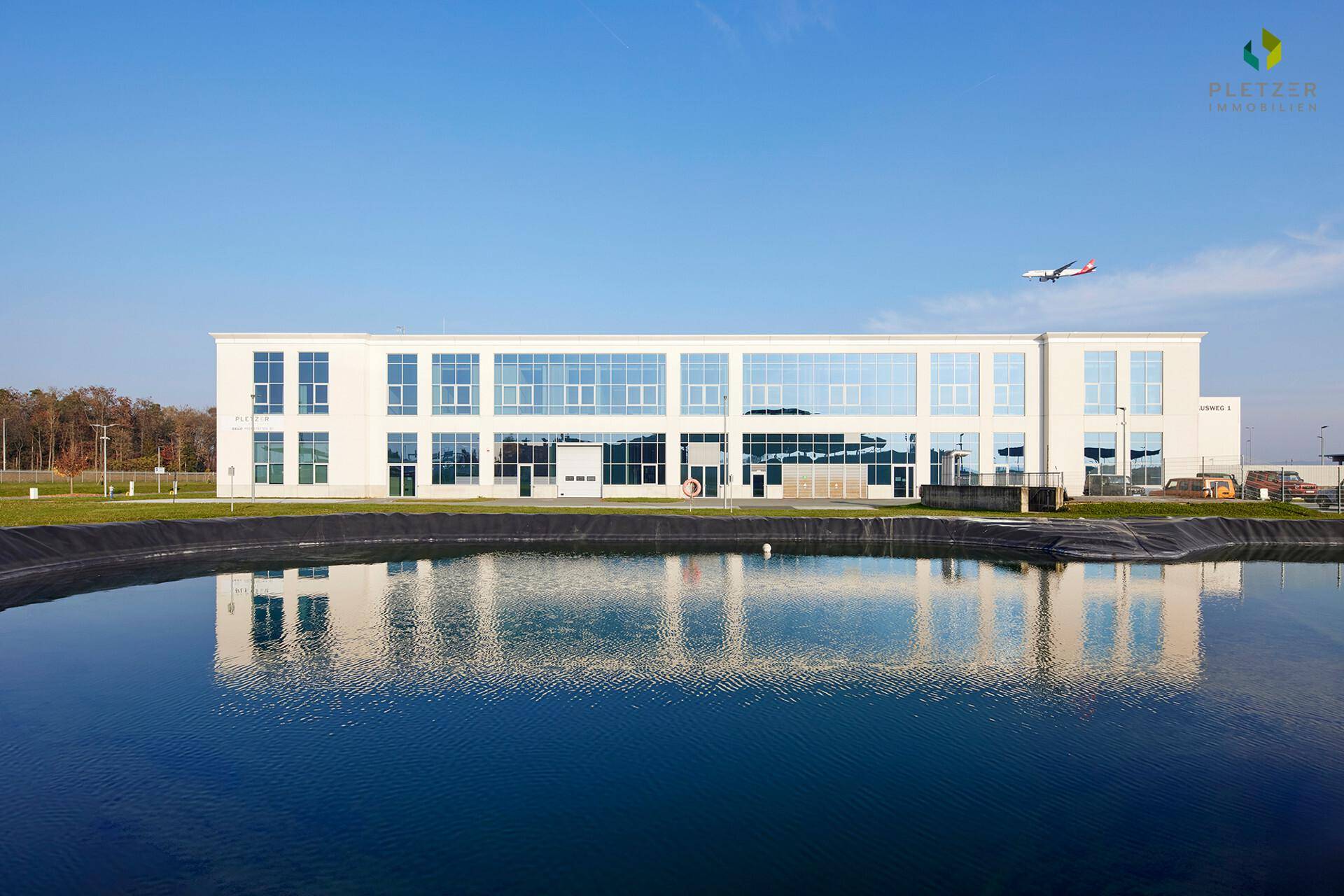 Modernes Geschäftsgebäude mit Glasfassade und Teich im Vordergrund unter blauem Himmel.