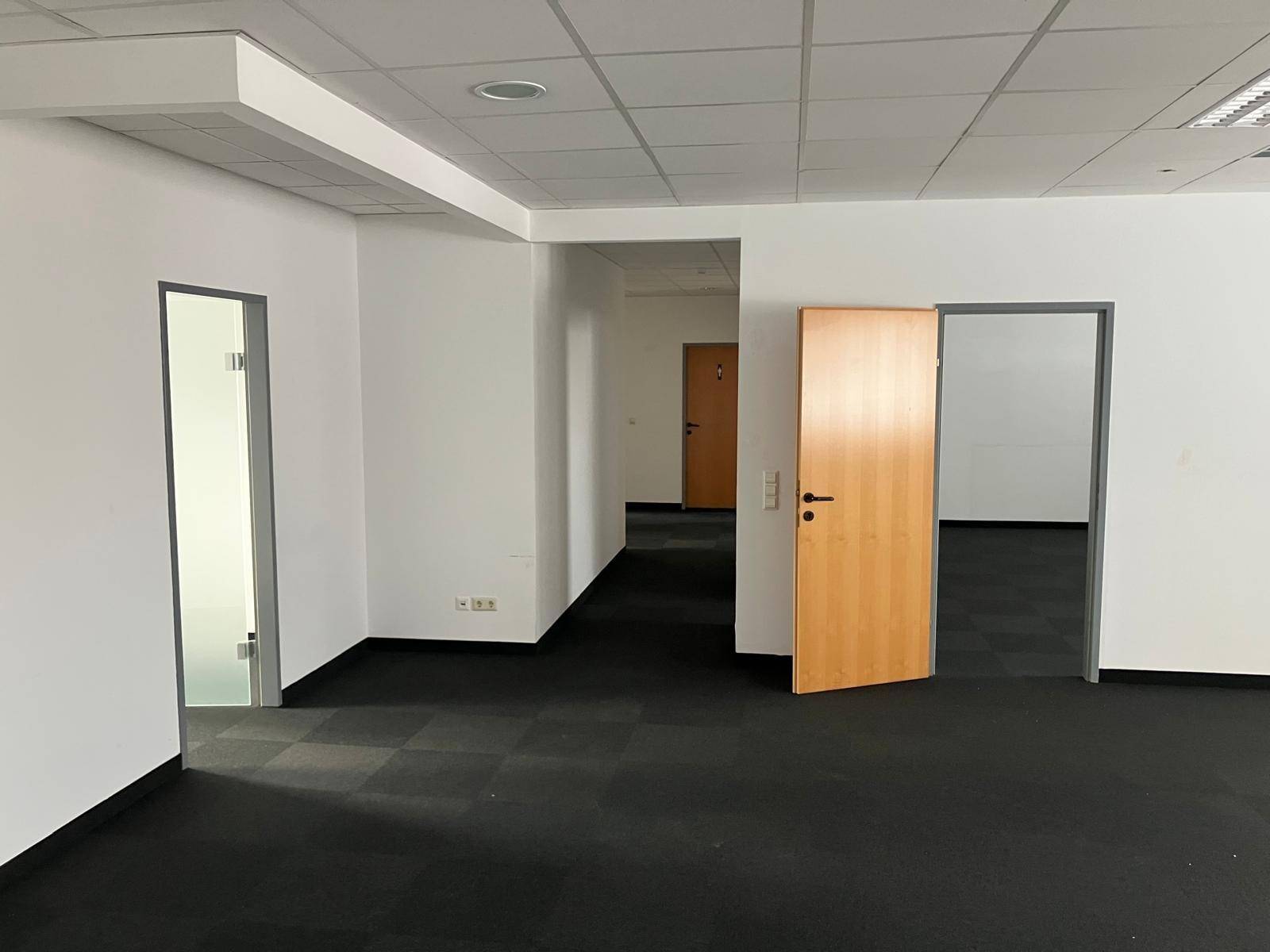 Geräumiges, leeres Büro mit dunklem Teppichboden und mehreren Türen, das eine flexible Raumgestaltung ermöglicht.